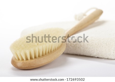 A bath brush is laying on folded, nature colored towel in front of a white background.