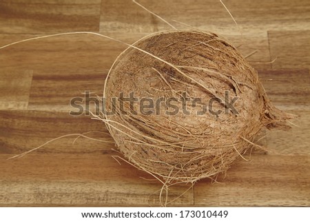A coconut is laying on a tabletop of acacia wood.