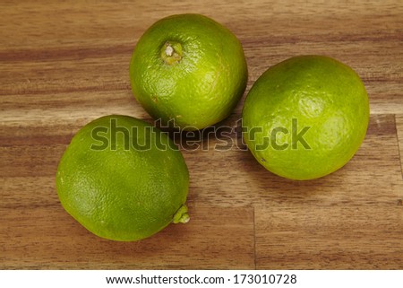 Three green limes are laying on a tabletop of acacia wood.