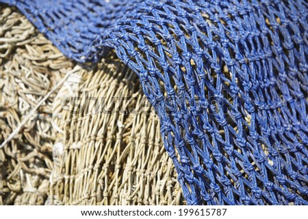A pile of old fishing nets made of natural fibre and blue synthetic fiber are laying in the harbor.