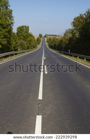 A hilly landscape with a straight road and bushes taken by fine weather with a cloudless blue sky.