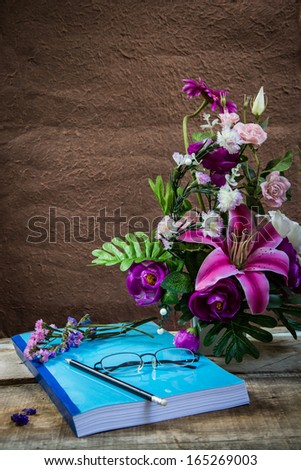 Flower and Yellow Glasses place on note books with flowers vase on wooden table.