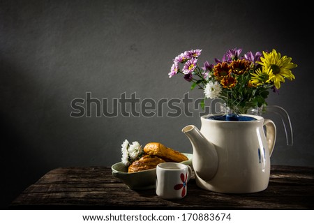 Still life of bread and tea and a vase of flowers on a background of old pictures.