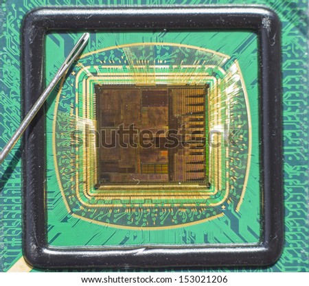 Open computer chip with gold wire connections compared to a needle
