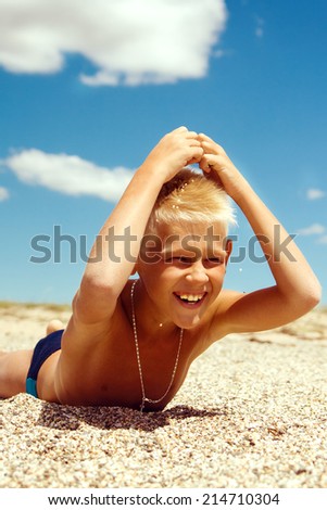 boy laughs and throws sand on his head lying on the sand against the blue sky
