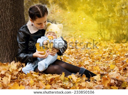 Mother keeps son in his arms while sitting in the autumn park near tree
