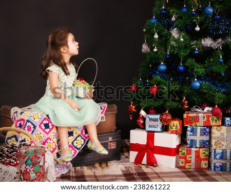 dark-haired girl sitting and looking up at the Christmas tree