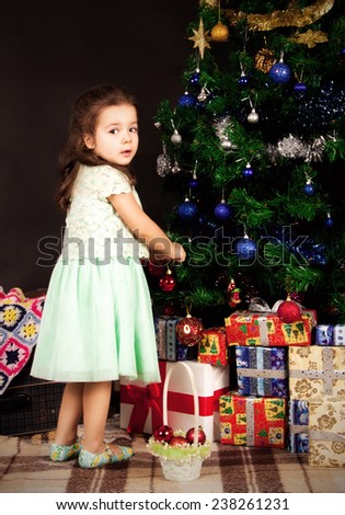 dark-haired girl standing near the Christmas tree and hang toys looking away