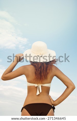 girl in a bathing suit and hat standing with his back against the blue sky