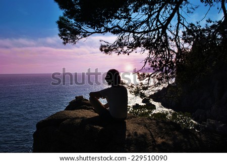 silhouette man sits on top and admire the sunset and the sea