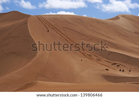 Group of bikers descend a steep sand dune in the Sahara Desert of Morocco in North Africa