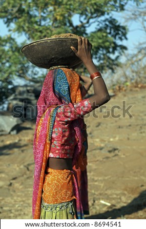 Indian woman laborer wearing colorful sari carrying a metal bowl filled with earth