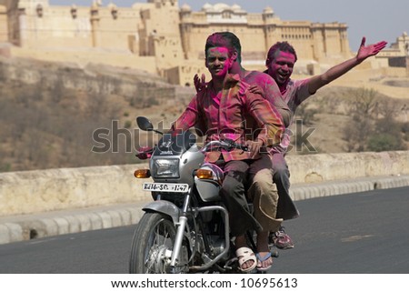 Group of young Indians on a motorbike covered in coloured paint from celebrating the Hindu Festival of Holi. Amber Fort in the background.