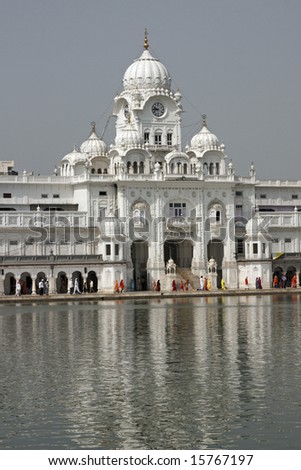 Golden Temple. Holiest shrine of the Sikh religion. Pilgrims walking in front of a white building with dome on the edge of an artificial lake, Amritsar, Punjab, India.