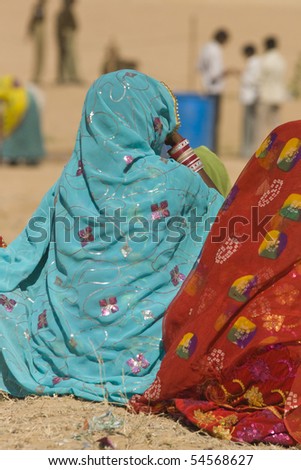 Ladies in brightly colored saris sitting on the ground watching events at the Desert Festival in Jaisalmer, Rajasthan, India