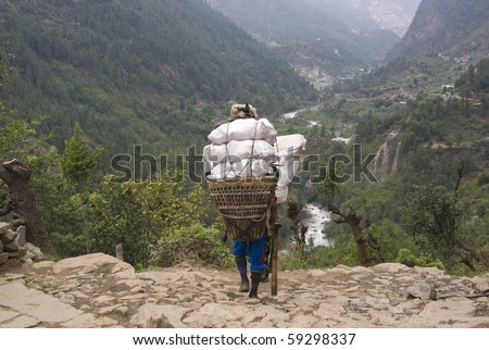 Porter carrying a very heavy load along a path in the Himalaya Mountains, Nepal