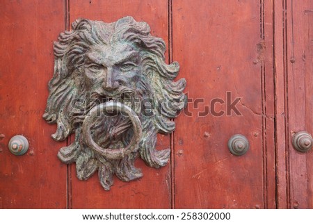 Large metal door knocker in the shape of a mans head with long flowing hair on a wooden door in the historic old city of Cartagena de Indias, Colombia