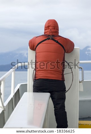 A man in a down parka stands on the bow of a day cruise boat in Alaska\'s Kenai National Park