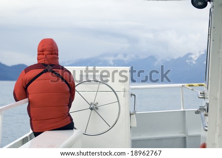 A man in a down parka sits on the bow of a day cruise boat in Alaska\'s Kenai National Park