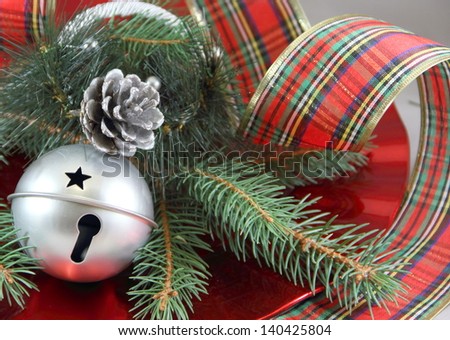 Silver Bell and Ribbon Silver sleigh bell and pine cone, with fresh cut pine. Wide plaid curled ribbon surrounding the red dish.