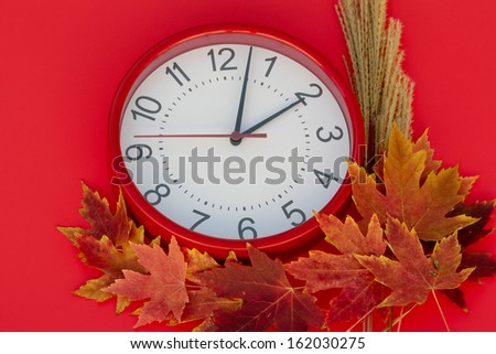 Daylight Saving Clock Red clock set at 2 a.m.  To the bottom and right of the clock are colorful fall leaves placed on a red background.