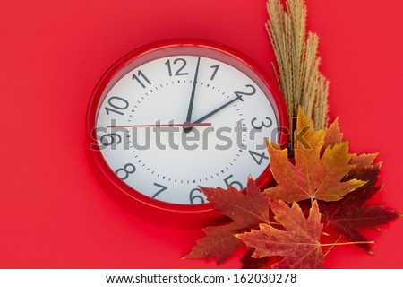 Fall Daylight Saving Red clock set a little after 2 a.m.  On the right side of the clock there are autumn leaves. The background of the image is red.