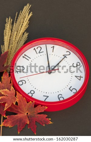 Daylight Saving Red clock set a 2 a.m.  Surrounding the clock are gorgeous fall leaves with a black background.