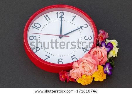 Daylight Saving Floral Spring time daylight saving clock and floral arrangement.  The clock is red with black numbers, there is a spring floral arrangement next to the clock, in the bottom right side.