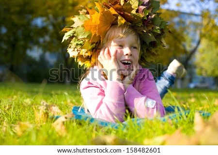 Attractive six year old girl in a wreath of autumn leaves lying on the grass