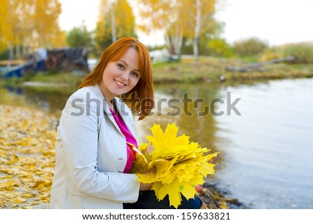 Portrait of the beautiful romantic woman with autumn leaves about a reservoir