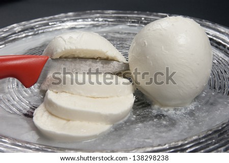 Mozzarella, typical fresh Italian cheese made with buffalo or cow milk in glass dish on a black background