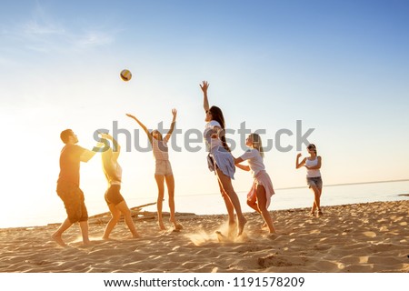 Group of happy friends plays with ball at sunset beach. Weekend activity concept