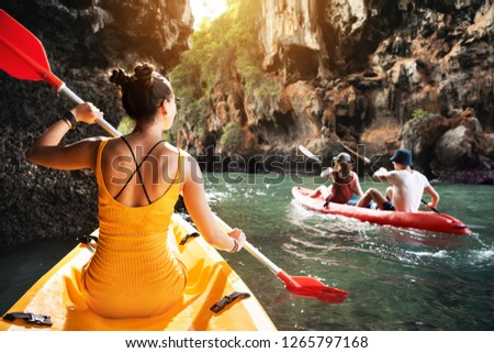 Beautiful lady and friends walks by kayaks at sea bay between big rocks