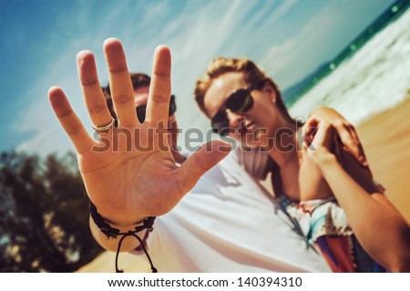 Cool guy and a girl in sunglasses are hugging and guy closes the camera by hand