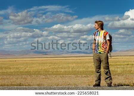 Man with backpack standing on the road on a background of mountains and desert