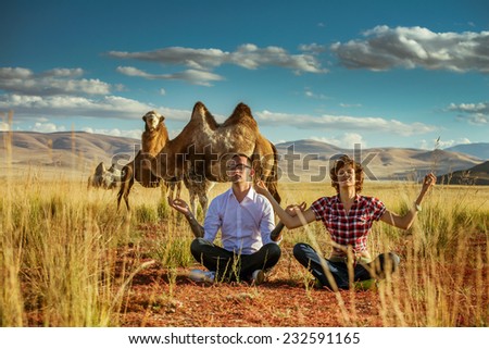 Happy couple sits in lotus position on the background of a big camel