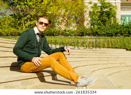 Fashion man in sunglasses, jacket and jeans is sitting on stairs