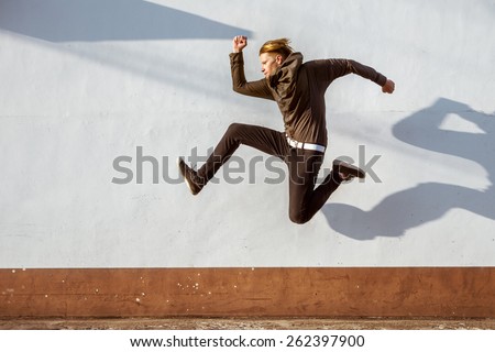 Man with funny long shadow jumps on background of white wall