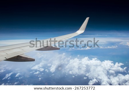 View from airplane window to the white wing and clouds in the sky. View from high altitude
