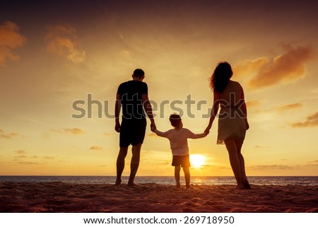 Happy family standing on the background of the sunset sky and sea holding hands