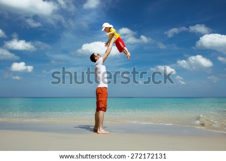 Happy father throws up his son on background of tropical beach