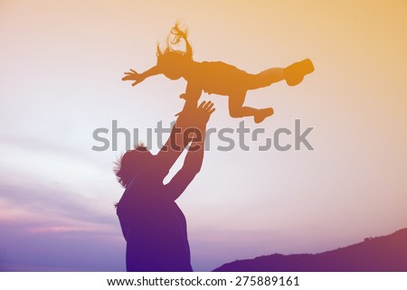 Silhouettes of happy family of father and daughter are playing on sunset background. Father throws up daughter