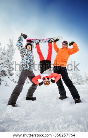 Group of three friends having fun holding girl snowboarder flipped upside down. Sheregesh resort, Siberia, Russia