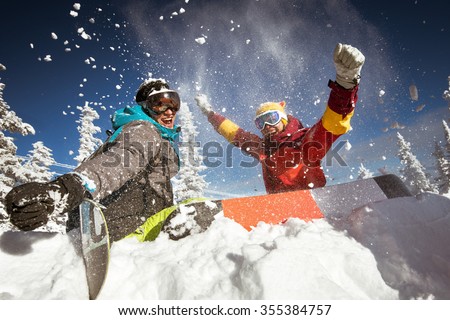 Happy couple of snowboarders having fun sitting in snowdrift with snowboards and