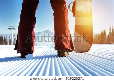 Snowboarder stands on slope backdrop. Closeup legs and snowboard