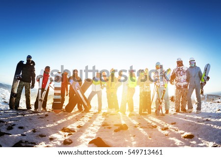 Winter sports concept with group of friends. Skiers and snowboarders stands on sunset backdrop