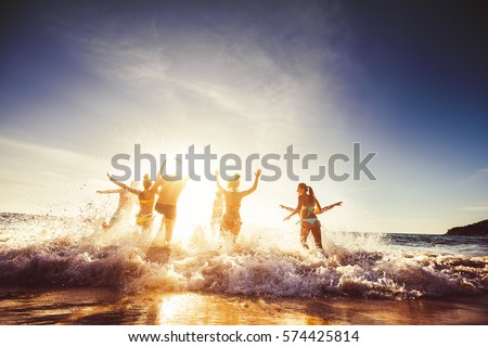 Big group of friends runs in sun light at the beach into the sea. Travel concept. Space for text