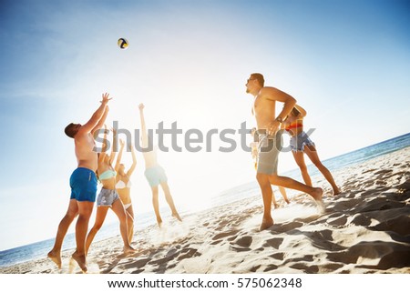 Group of friends playing game with ball at the beach on background of sunset sea