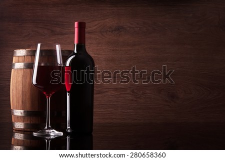 Bottle of red wine, glass and barrel on dark wooden background
