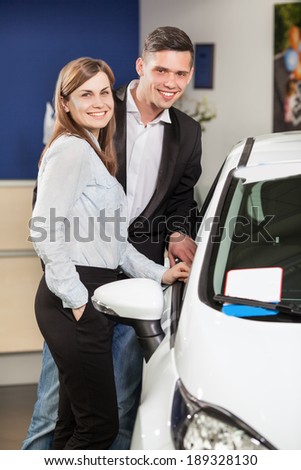 This car is exactly what we want. Beautiful young couple standing at the car dealership and making their decision